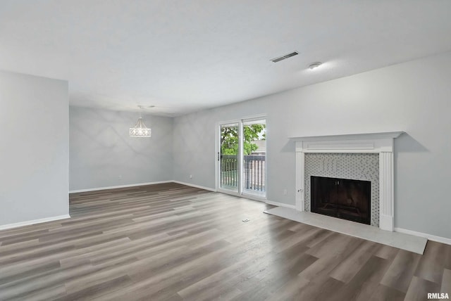unfurnished living room with a tiled fireplace, wood finished floors, a chandelier, and baseboards