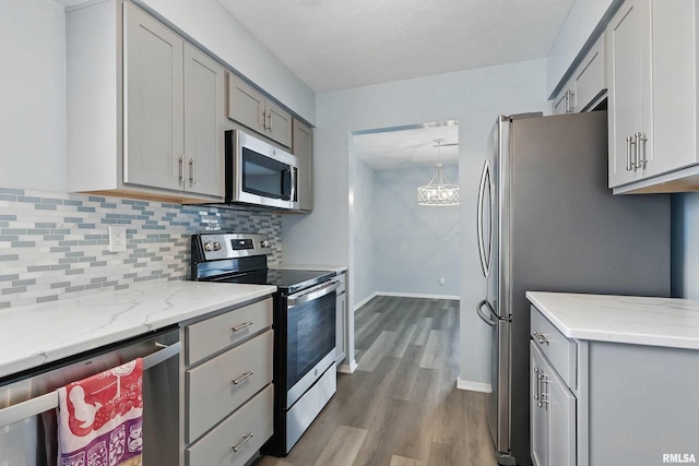 kitchen featuring appliances with stainless steel finishes, gray cabinets, wood finished floors, and backsplash