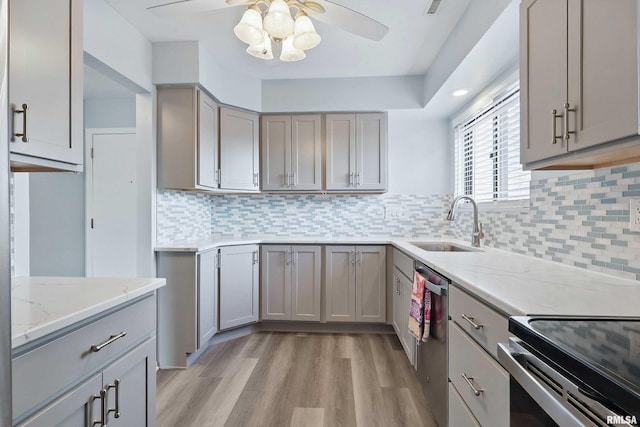 kitchen featuring a sink, gray cabinetry, light wood-style floors, ceiling fan, and light stone counters