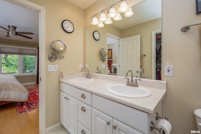 ensuite bathroom featuring ceiling fan, double vanity, and baseboards