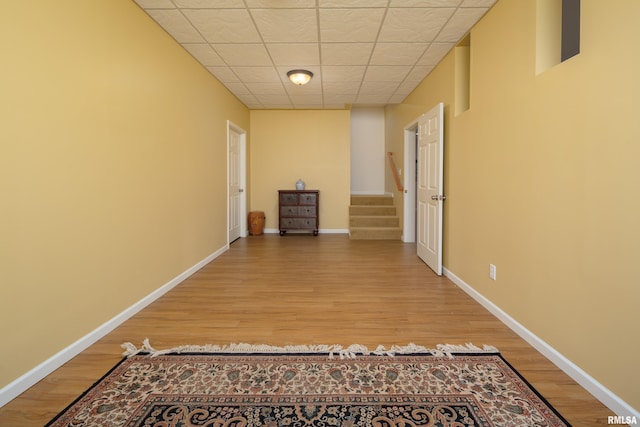 hall featuring light wood-type flooring, stairway, baseboards, and a drop ceiling