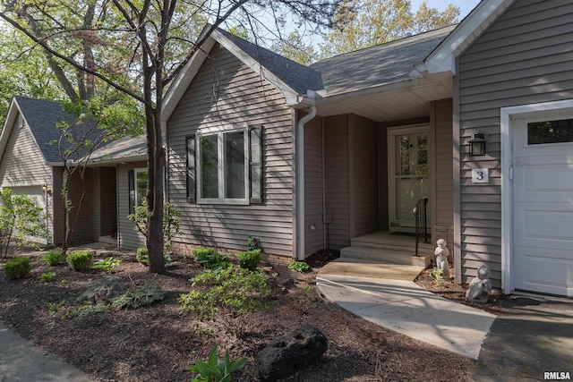 entrance to property with roof with shingles and an attached garage