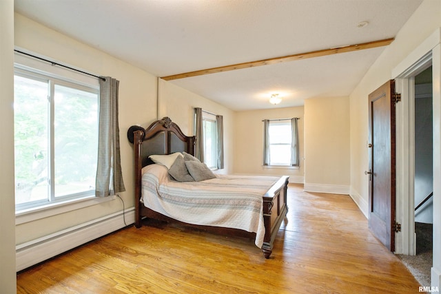 bedroom with a baseboard heating unit, light wood-type flooring, and baseboards