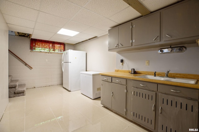kitchen with gray cabinetry, freestanding refrigerator, fridge, a sink, and a drop ceiling