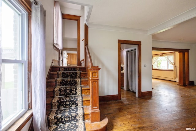 stairway featuring baseboard heating, ornamental molding, wood finished floors, and baseboards