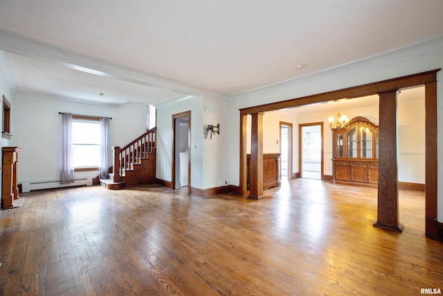 unfurnished living room with baseboard heating, a chandelier, hardwood / wood-style floors, ornamental molding, and ornate columns
