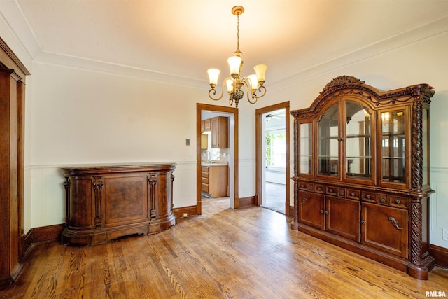 unfurnished dining area featuring a chandelier, light wood-style flooring, crown molding, a sink, and baseboards
