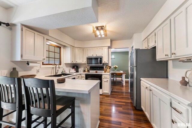 2115 W 31st St, Davenport, IA 52804 - kitchen with appliances with stainless steel finishes, a sink, a peninsula, dark wood-style floors, and a textured ceiling