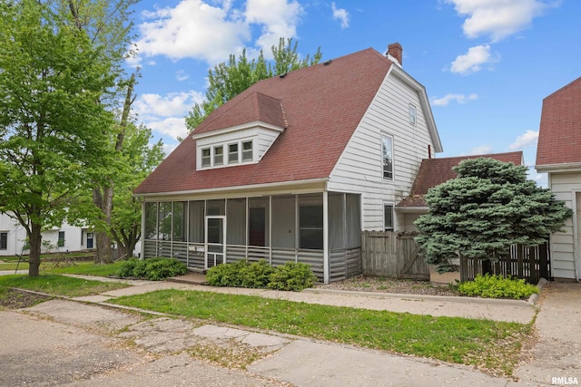view of front of property with a sunroom, a chimney, fence, and a shingled roof