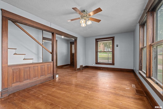 unfurnished room featuring hardwood / wood-style flooring, a textured ceiling, stairway, baseboards, and a ceiling fan