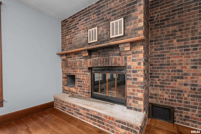 detailed view of baseboards, a brick fireplace, wood finished floors, and a textured ceiling