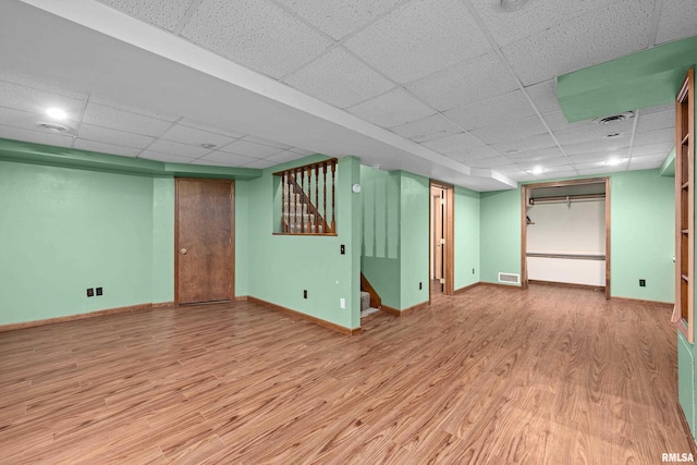 finished below grade area featuring a drop ceiling, wood finished floors, stairs, and baseboards