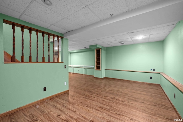 empty room with a paneled ceiling, wood finished floors, and baseboards