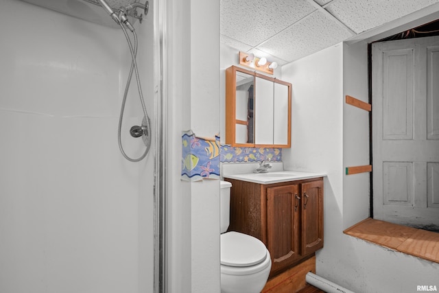 bathroom with a shower, a drop ceiling, toilet, vanity, and wood finished floors