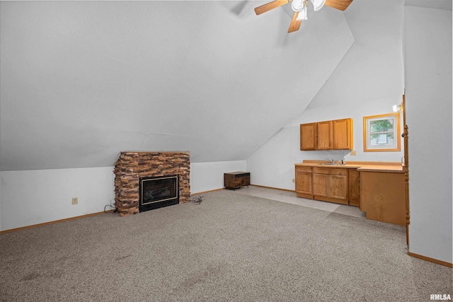 unfurnished living room featuring vaulted ceiling, ceiling fan, light colored carpet, baseboards, and a stone fireplace