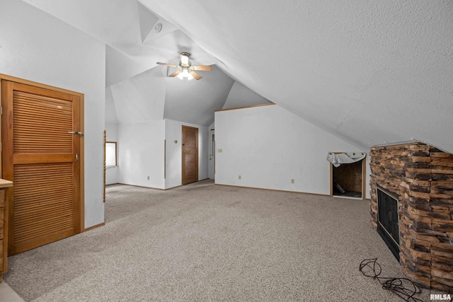 unfurnished living room featuring vaulted ceiling, ceiling fan, carpet flooring, a stone fireplace, and baseboards