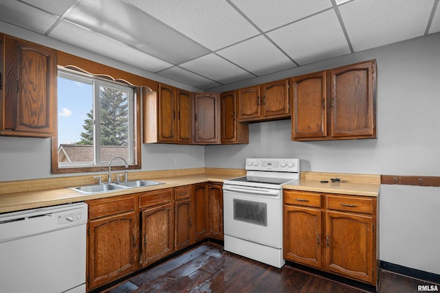 kitchen with white appliances, a sink, a paneled ceiling, light countertops, and dark wood-type flooring