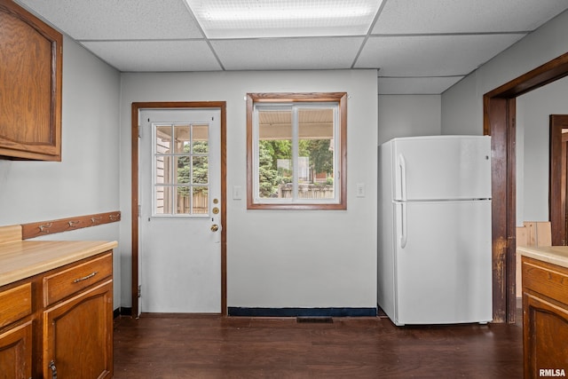 kitchen featuring freestanding refrigerator, a drop ceiling, light countertops, dark wood-style flooring, and brown cabinetry