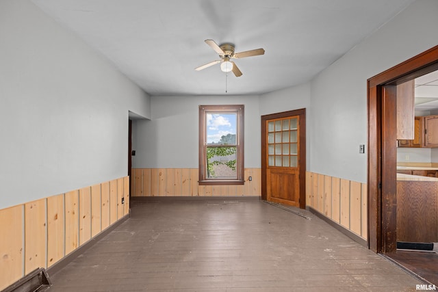empty room with wainscoting, wood walls, ceiling fan, and hardwood / wood-style flooring