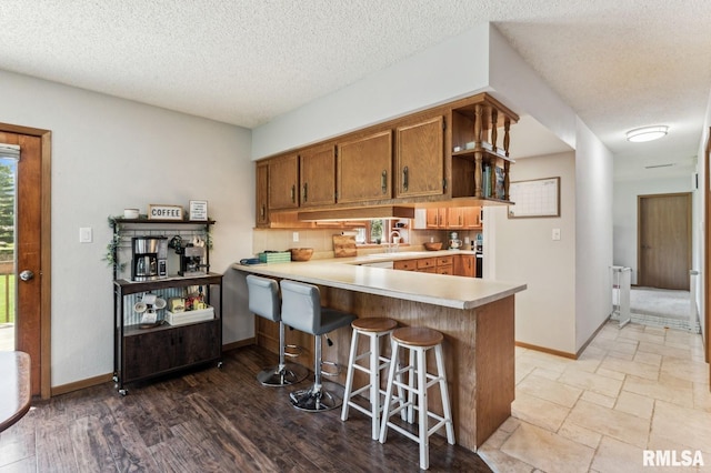 kitchen with light countertops, a peninsula, a textured ceiling, brown cabinetry, and baseboards