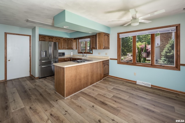 kitchen featuring stainless steel appliances, a peninsula, a sink, brown cabinetry, and light wood finished floors