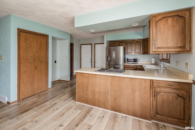 kitchen featuring stainless steel fridge, a sink, a peninsula, light wood-style floors, and baseboards