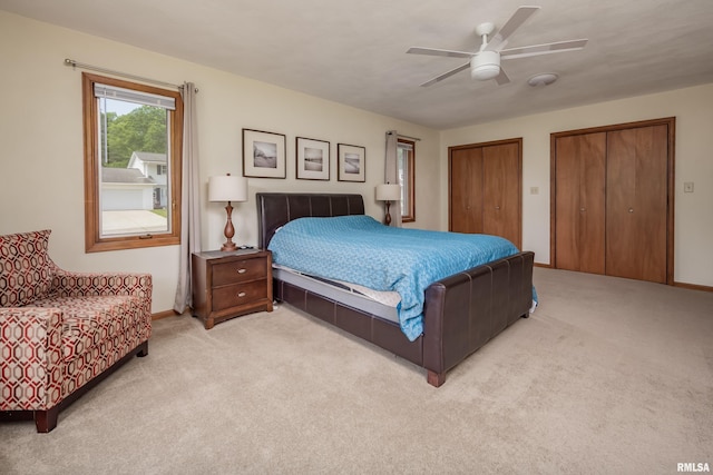 bedroom featuring light colored carpet, multiple closets, baseboards, and a ceiling fan