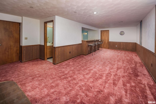 carpeted spare room with a wainscoted wall, wooden walls, bar, and a textured ceiling