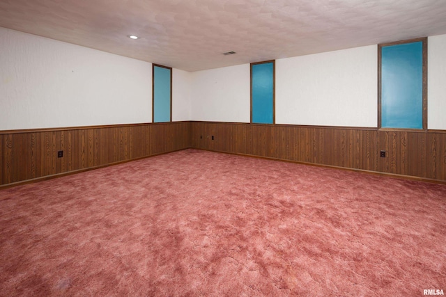 unfurnished room with wooden walls, a textured ceiling, a wainscoted wall, and carpet floors