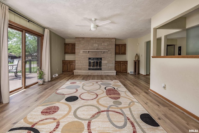 unfurnished living room with a ceiling fan, a textured ceiling, light wood finished floors, a fireplace, and baseboards