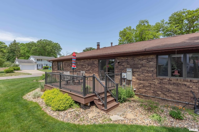 rear view of house with brick siding, a deck, a lawn, and roof with shingles