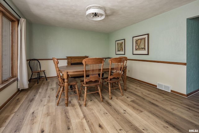 dining area with light wood finished floors, baseboards, and a textured ceiling
