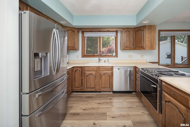 kitchen featuring stainless steel appliances, a sink, brown cabinets, light wood-style floors, and plenty of natural light