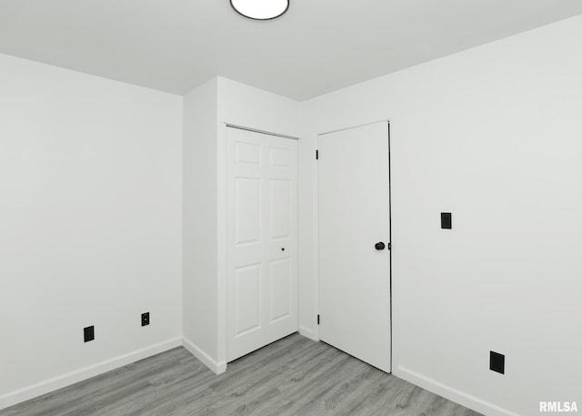 unfurnished bedroom featuring light wood-style flooring, baseboards, and a closet
