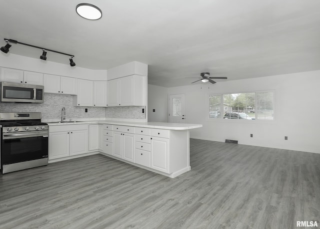 kitchen with stainless steel appliances, a peninsula, open floor plan, light countertops, and ceiling fan