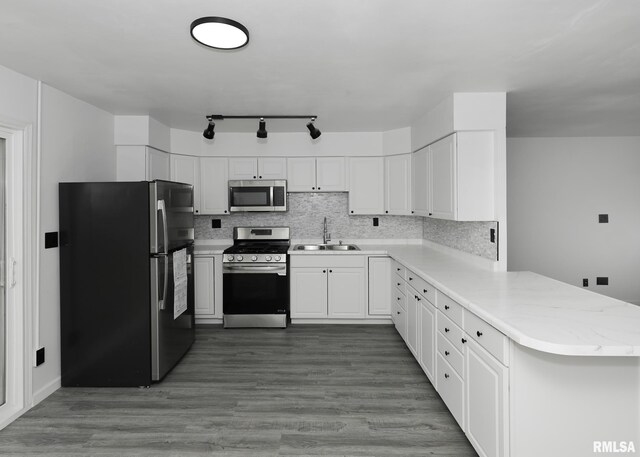 kitchen with appliances with stainless steel finishes, a sink, a peninsula, backsplash, and white cabinets