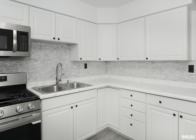 kitchen with stainless steel appliances, a sink, light countertops, backsplash, and white cabinetry