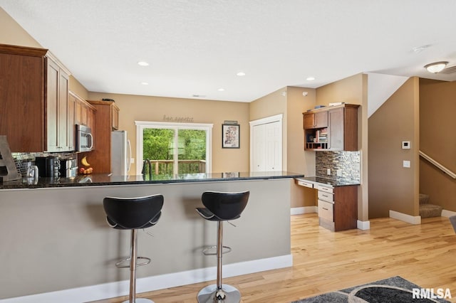 725 Cox Ct, Le Claire, IA 52753 - kitchen featuring stainless steel microwave, freestanding refrigerator, a peninsula, a breakfast bar, and tasteful backsplash