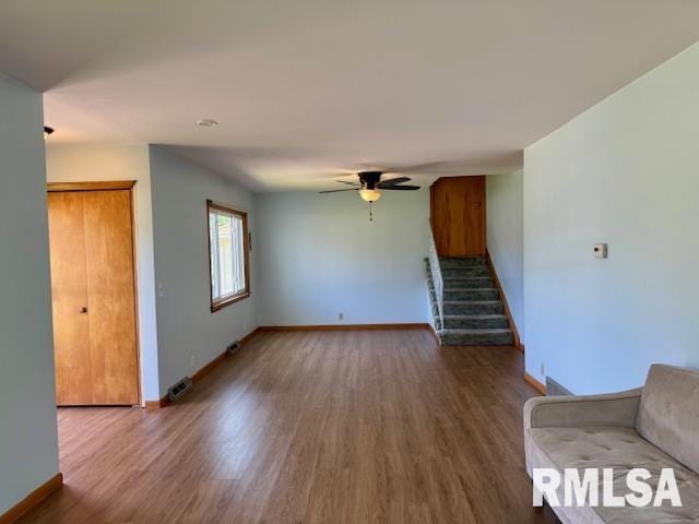 1003 16th Ave N, Clinton, IA 52732 - unfurnished living room with baseboards, stairs, wood finished floors, and ceiling fan