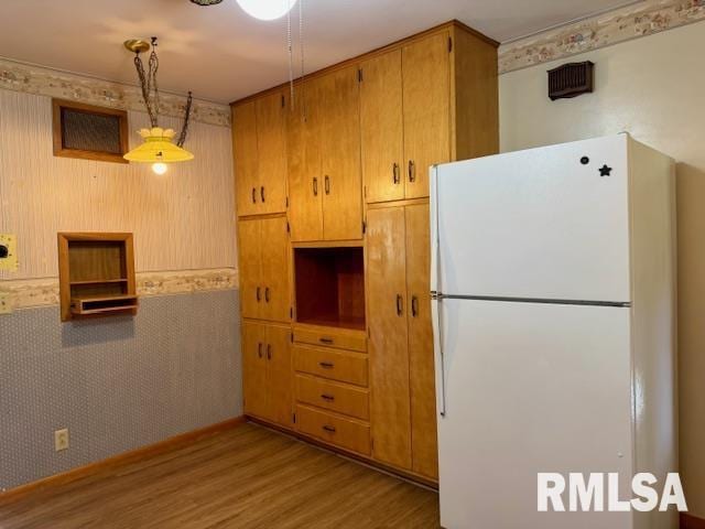 1003 16th Ave N, Clinton, IA 52732 - kitchen featuring freestanding refrigerator, wood finished floors, hanging light fixtures, and brown cabinets
