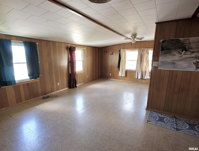 spare room with wooden walls, light flooring, a ceiling fan, and baseboards