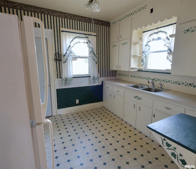 kitchen with a sink, light countertops, light flooring, wallpapered walls, and white cabinets