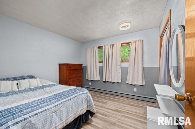bedroom with a baseboard radiator and light wood-style flooring