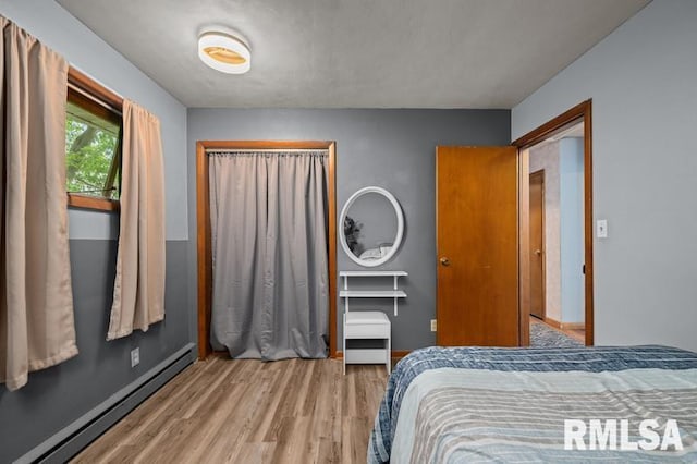 bedroom featuring a baseboard heating unit, light wood-style floors, baseboards, and a closet