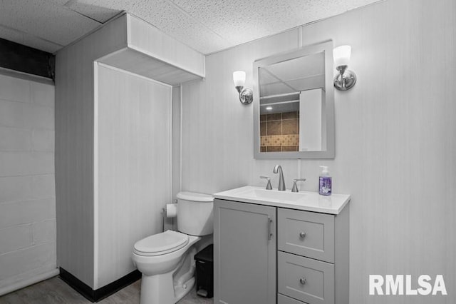 bathroom with toilet, wood finished floors, vanity, and a drop ceiling