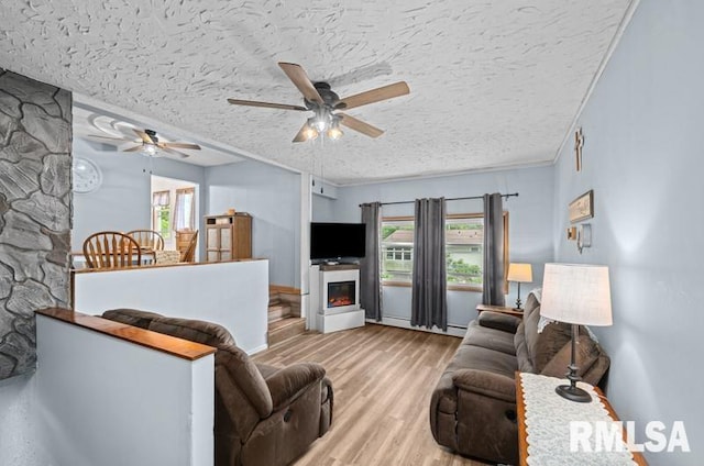 living room featuring a ceiling fan, wood finished floors, a warm lit fireplace, plenty of natural light, and a textured ceiling