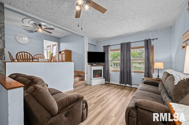 living area with ceiling fan, wood finished floors, a fireplace, a textured ceiling, and baseboard heating