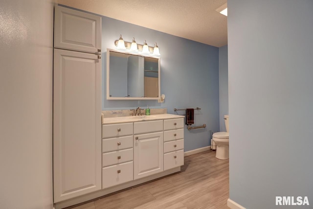 bathroom featuring toilet, wood finished floors, baseboards, vanity, and a textured ceiling