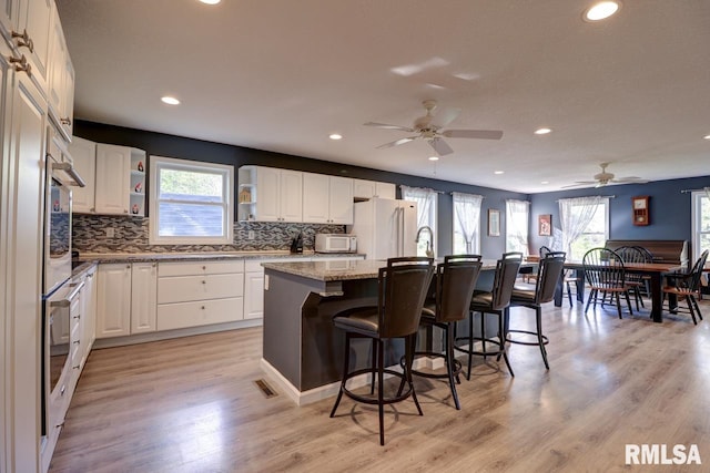 kitchen with freestanding refrigerator, ceiling fan, healthy amount of natural light, a breakfast bar area, and recessed lighting