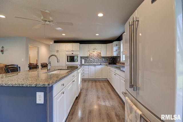 kitchen featuring white appliances, a sink, open shelves, light wood-style floors, and white cabinetry